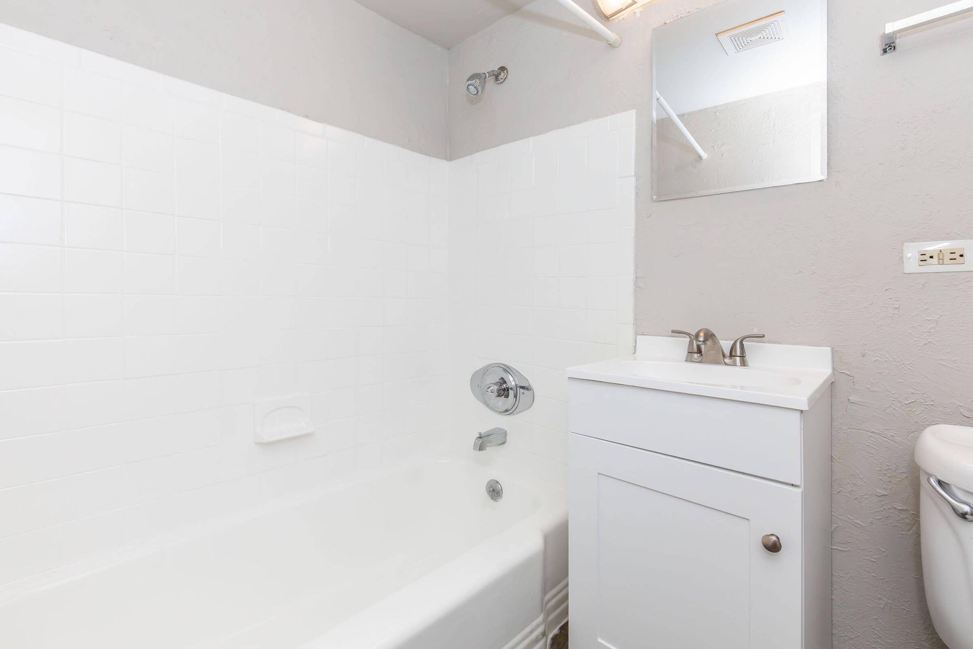 White bathroom with a bathtub, vanity, and mirror. Gray walls.