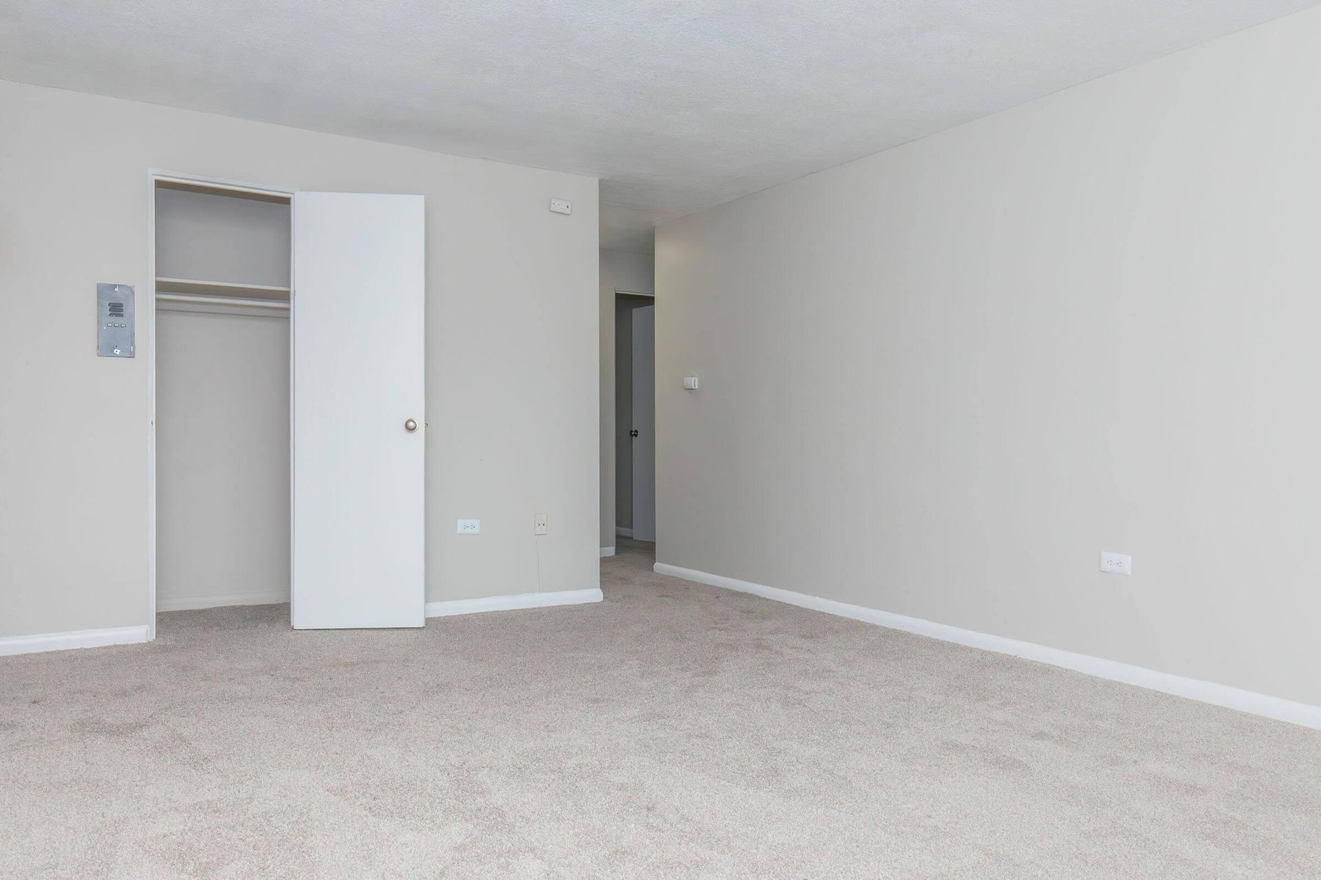 Empty room with beige carpet, white walls, and a closet with the door partially open.