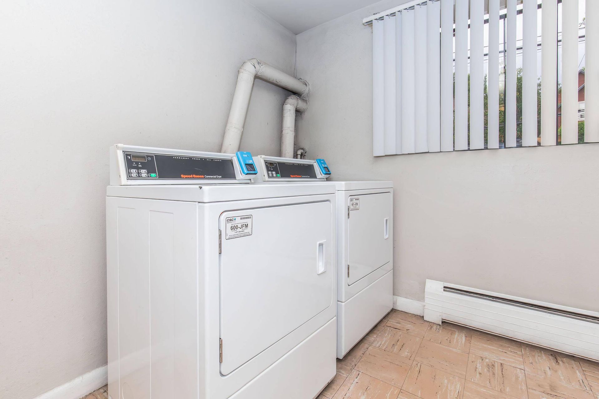 Two white dryers in a laundry room, with a window and vent pipes.