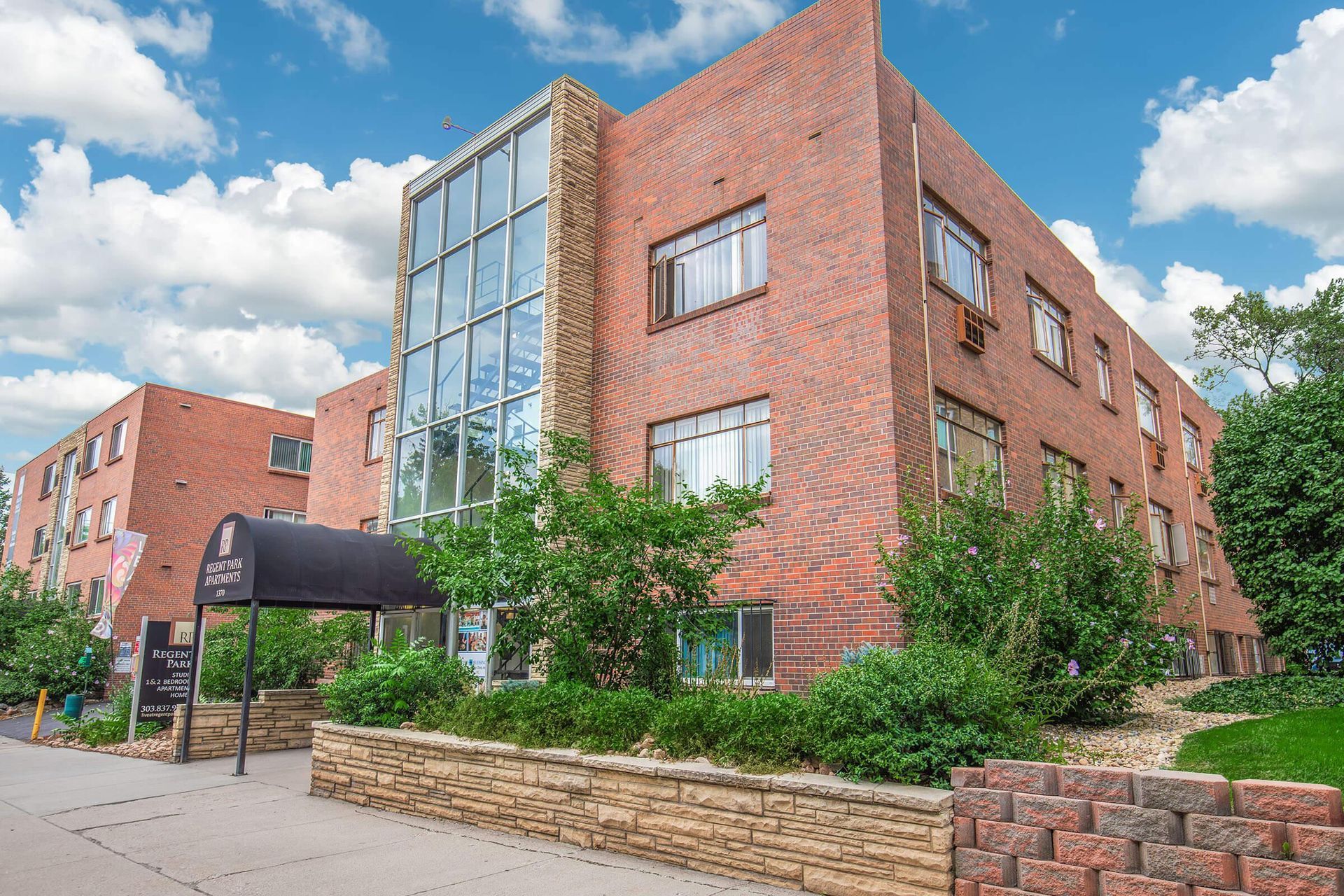 Brick apartment building with glass facade, black awning, and landscaped front.