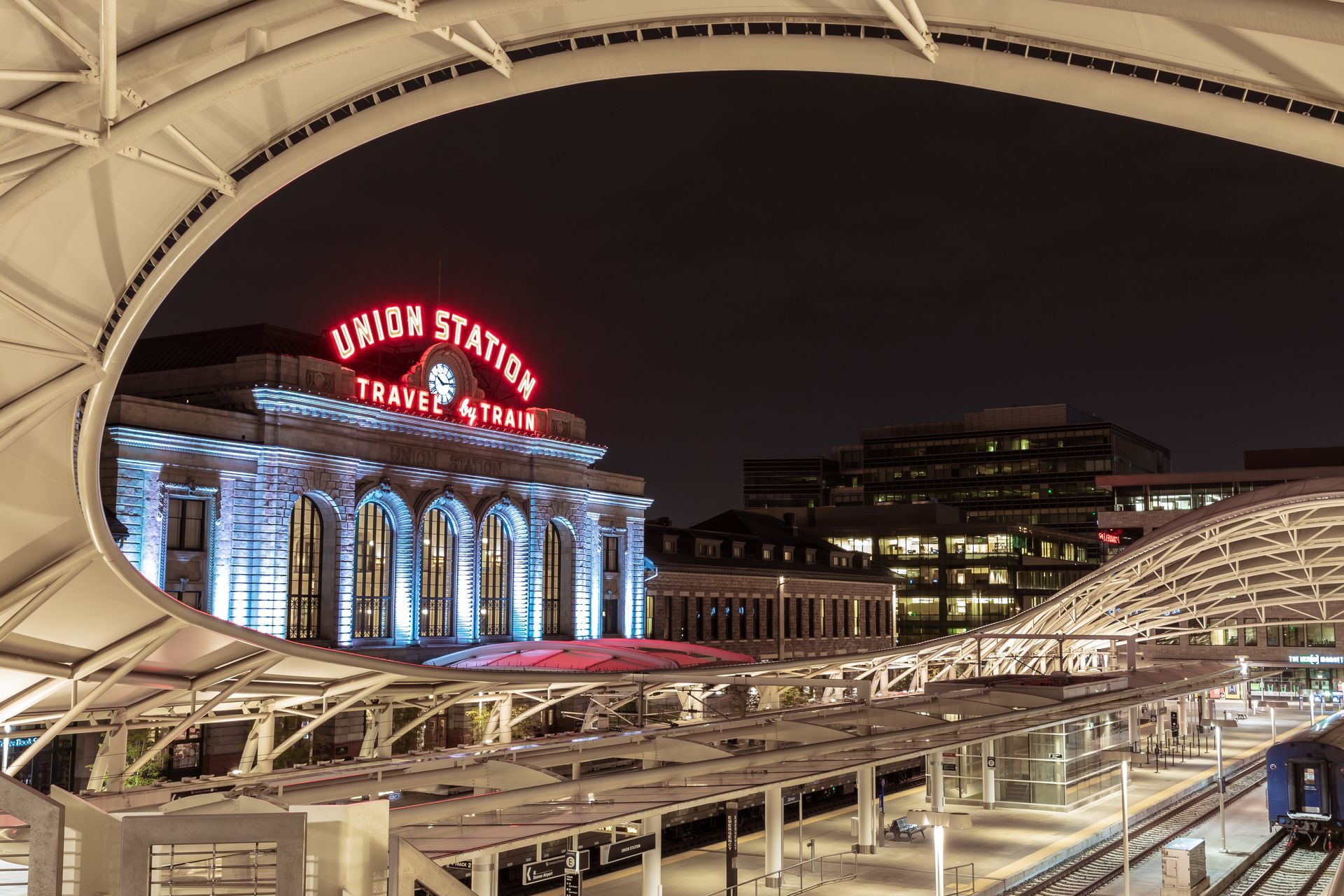Denver's Union Station lit up at night, with train tracks and modern canopy in the foreground.