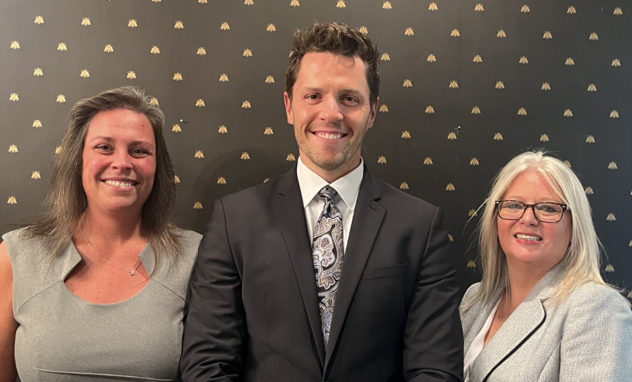 Three people in business attire smiling in front of a black and gold patterned wall.