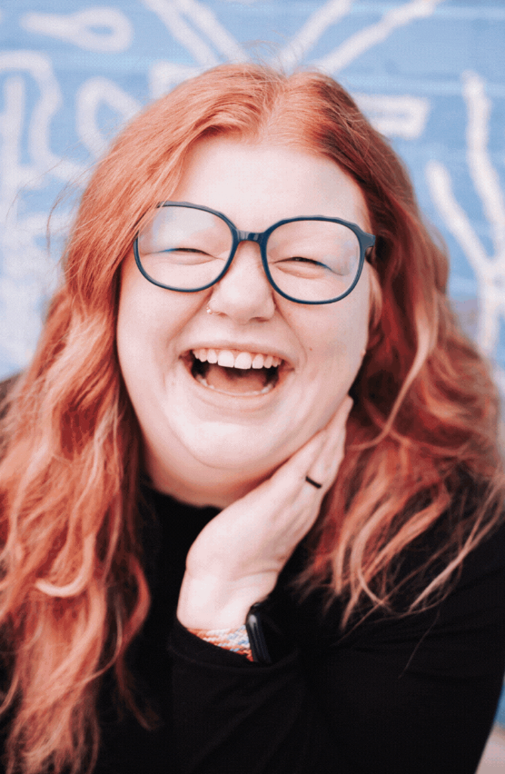 A woman wearing glasses is laughing with her hand on her face.