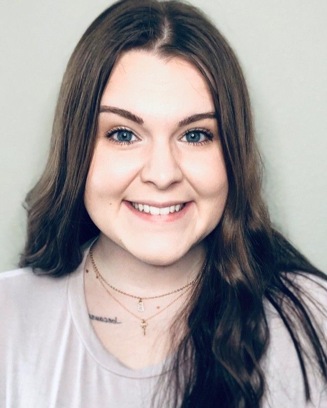 A woman wearing a white shirt and a necklace is smiling for the camera.