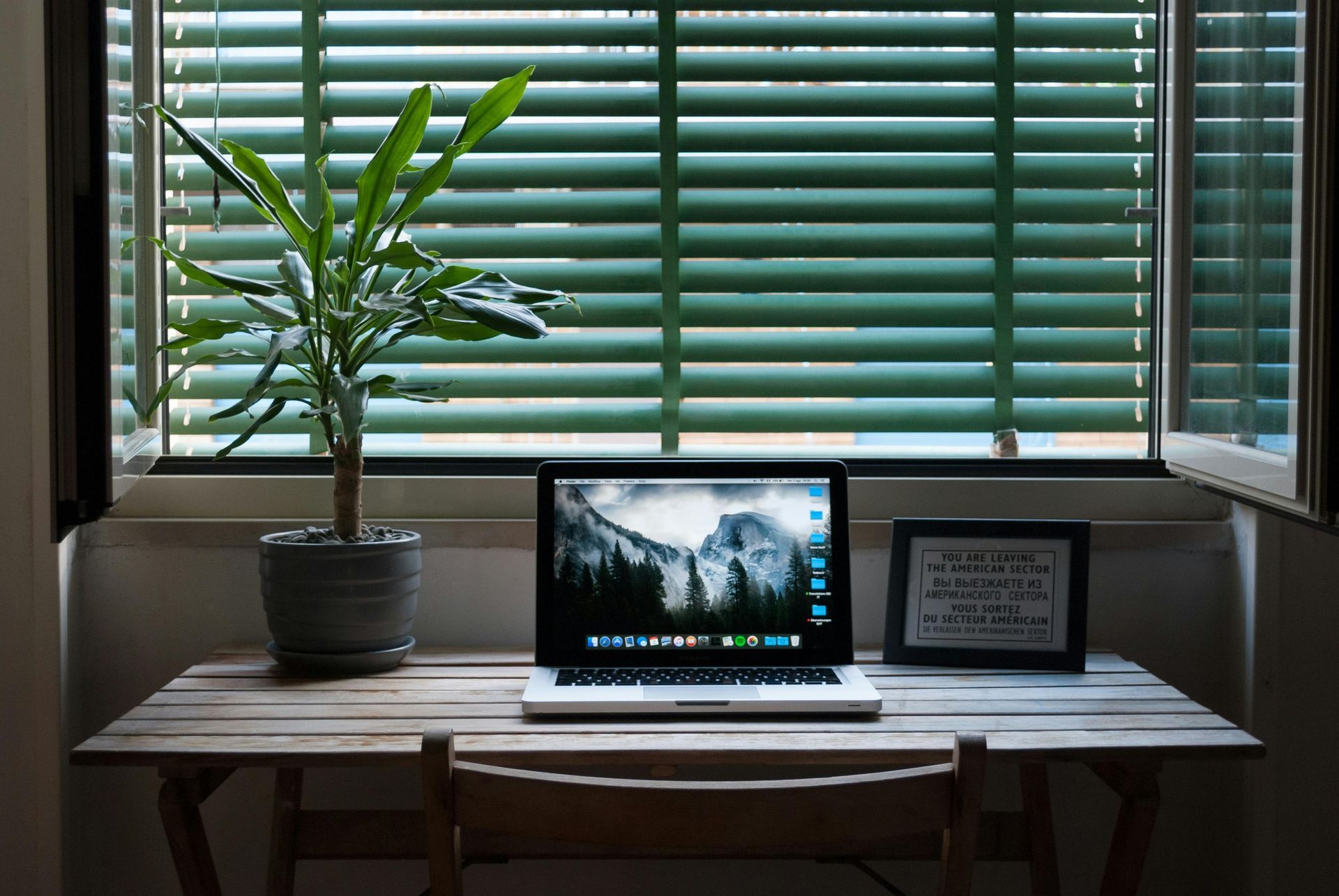 desk in front of window with blinds with a laptop open on desk