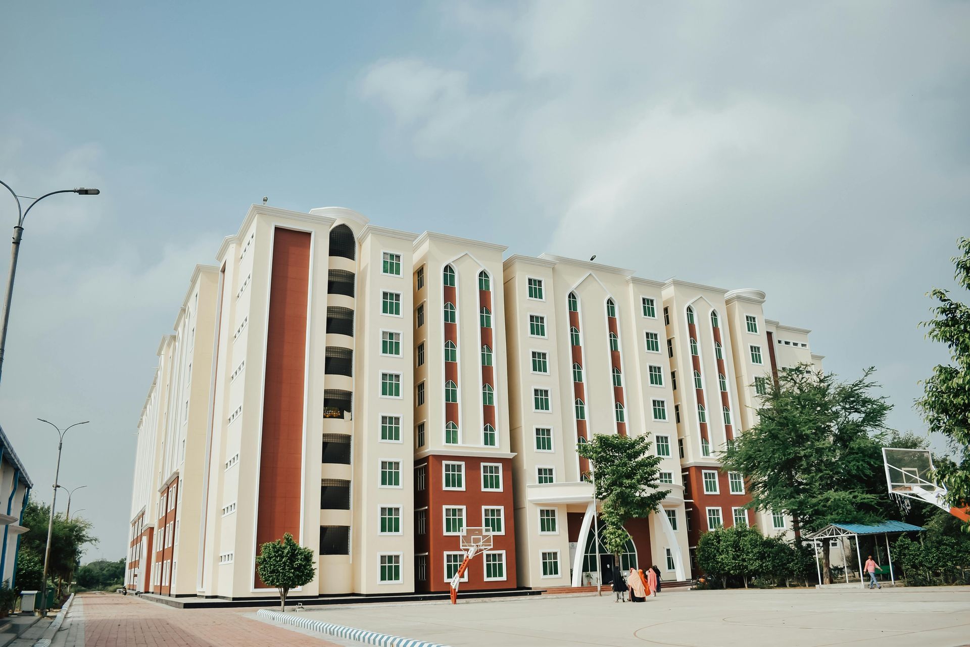 Large beige and red multi-story building with many windows under a cloudy sky.