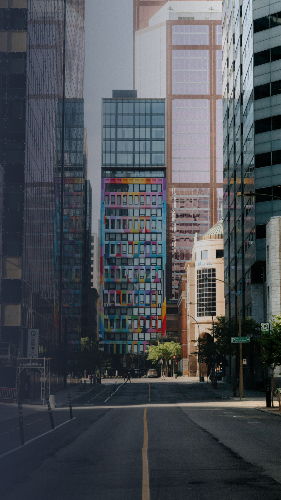 City street view: tall buildings flank a road with yellow lines, a colorful tower in the center.