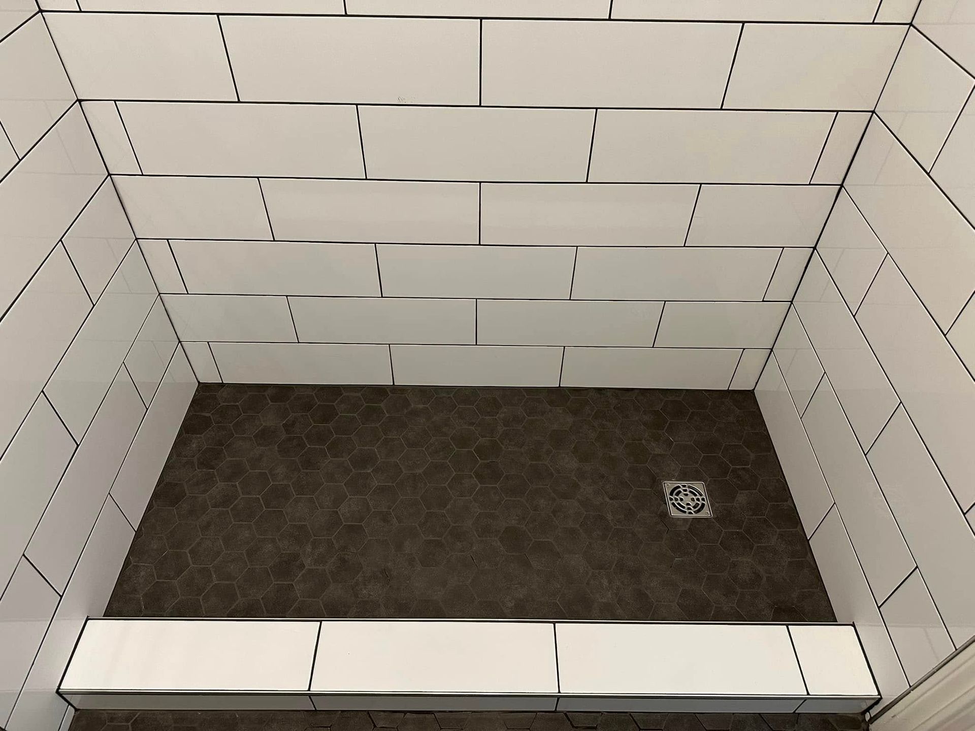 A shower stall with white tiles and a black floor