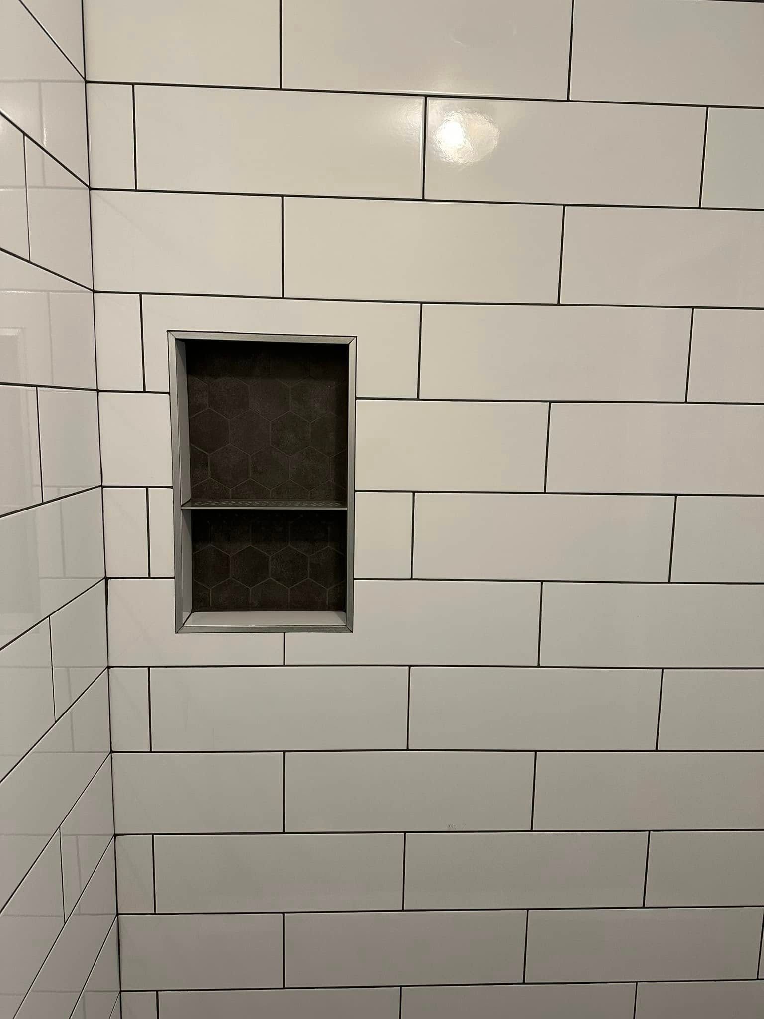 A shower stall with white tiles and a shelf in the corner.