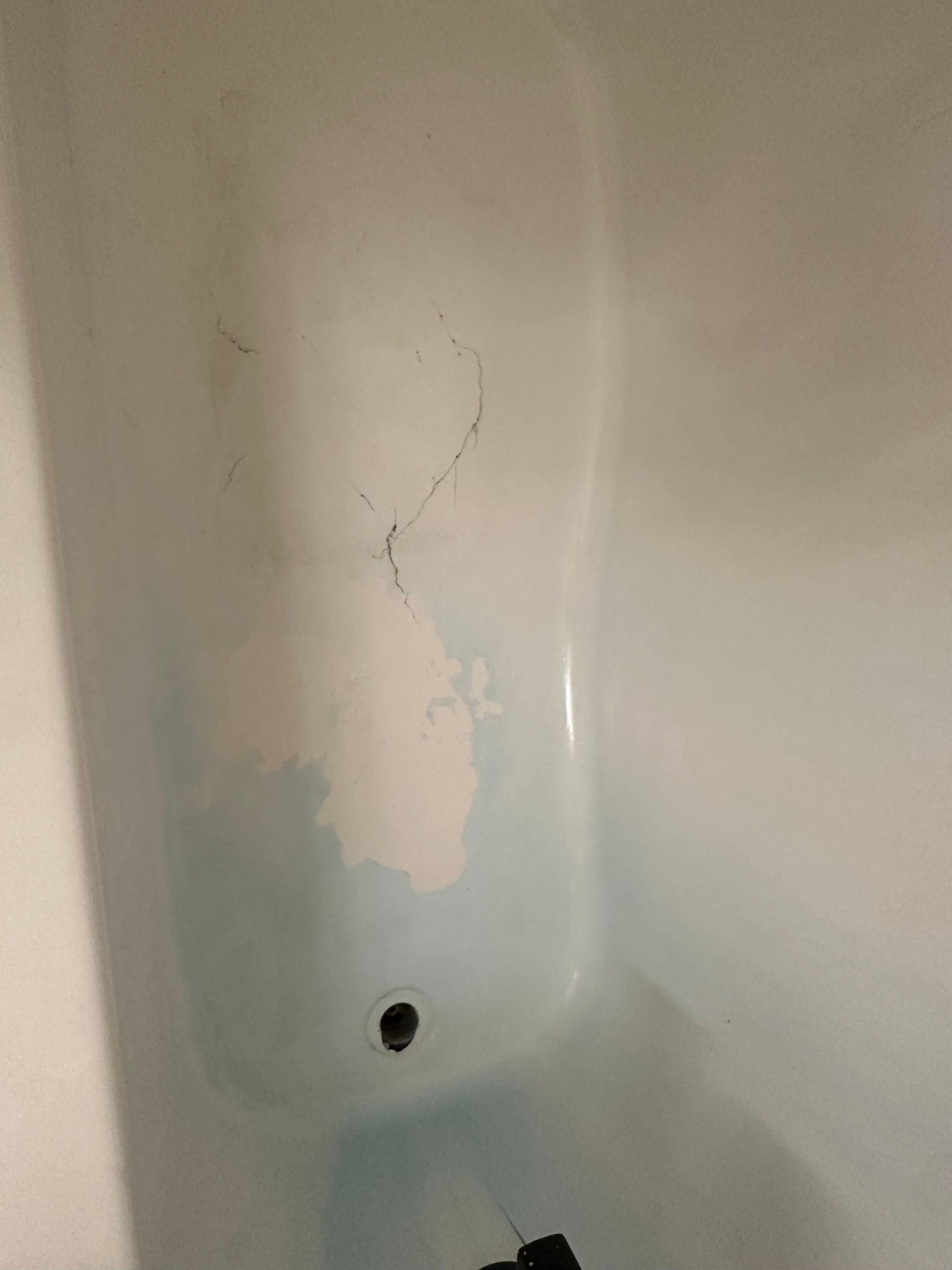 A bathtub with a hole in the wall and a drain.