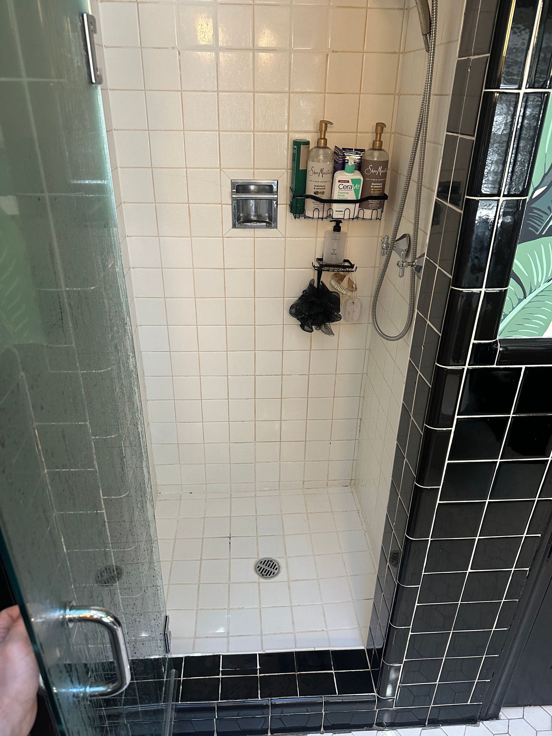 A shower with black and white tiles and a glass door.