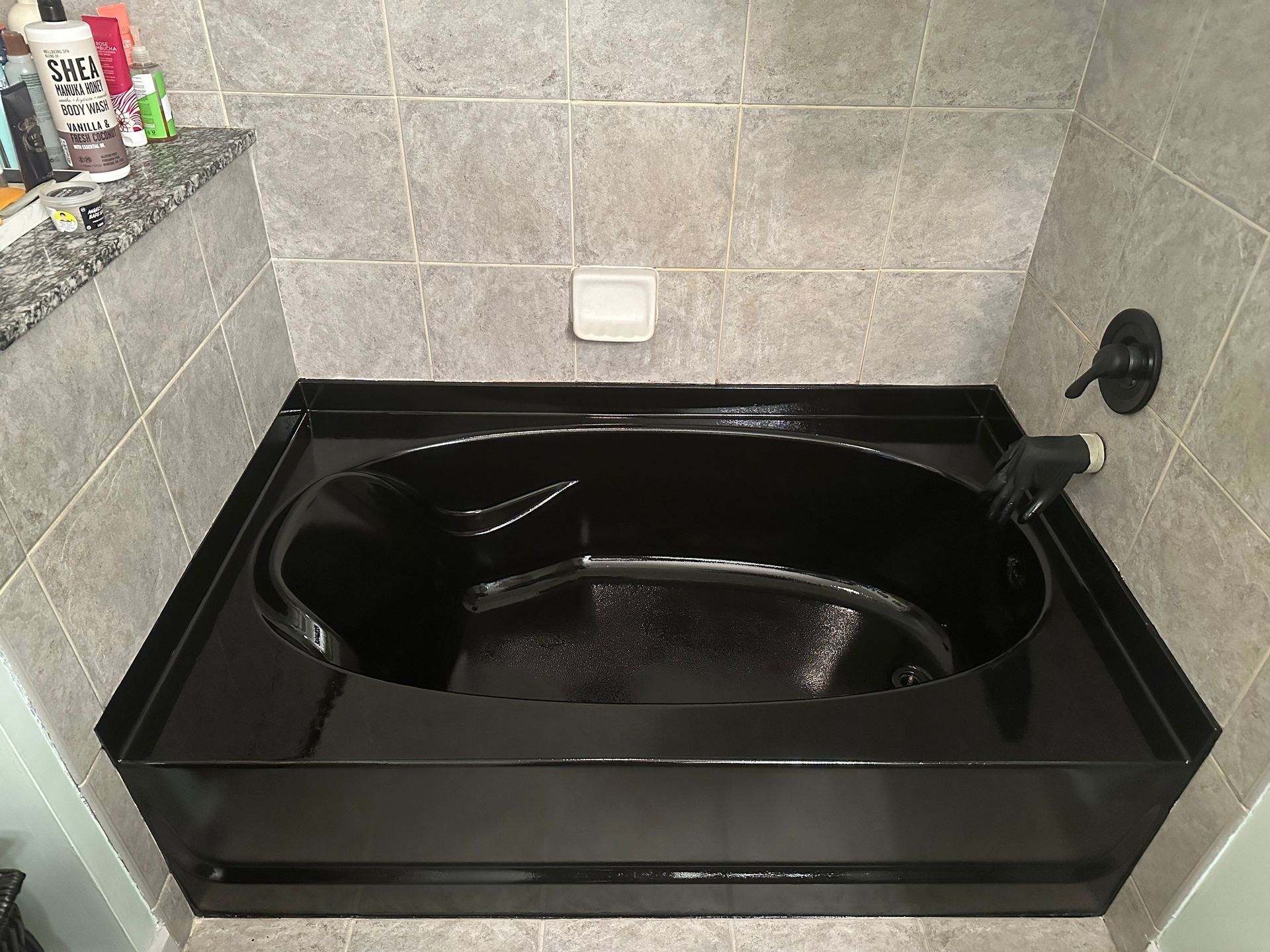 A black bathtub is sitting in a bathroom next to a tiled wall.