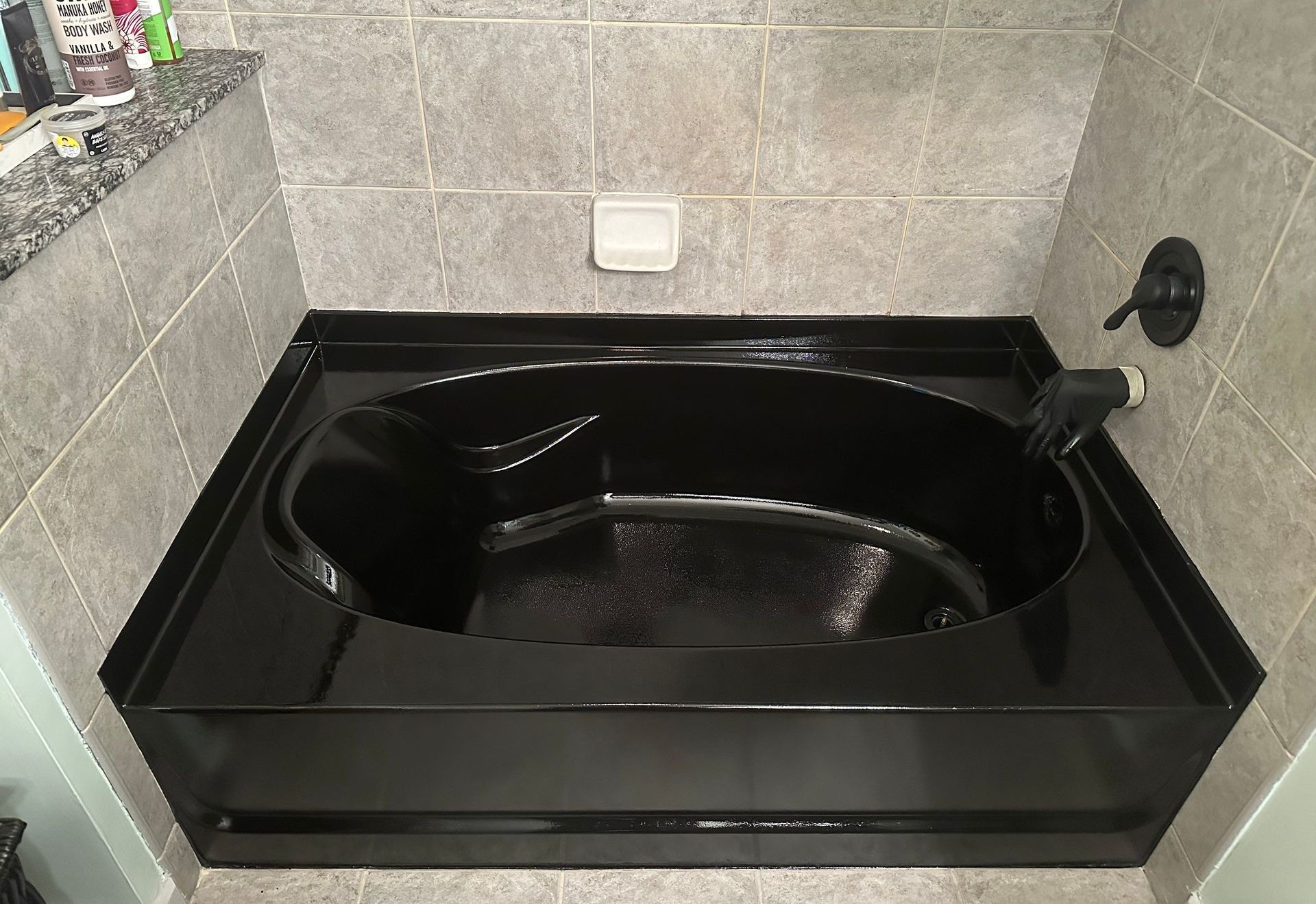 A black bathtub is sitting in a bathroom next to a tiled wall.