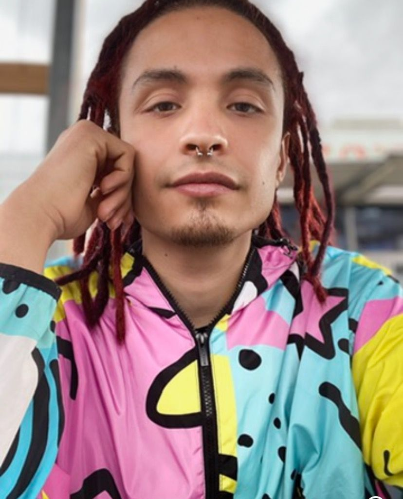 A man with dreadlocks is wearing a colorful jacket.