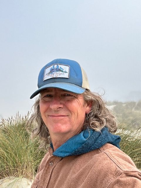 A man with long hair is wearing a blue hat and a brown shirt.