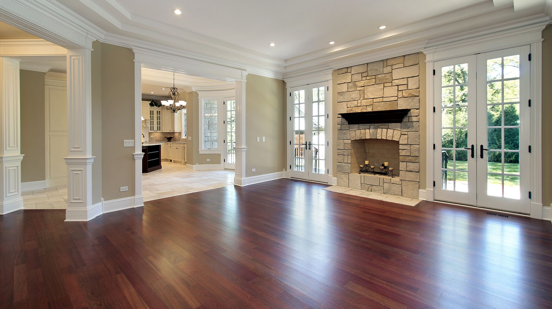 Spacious room with dark wood floor, stone fireplace, french doors, and a view to the kitchen.