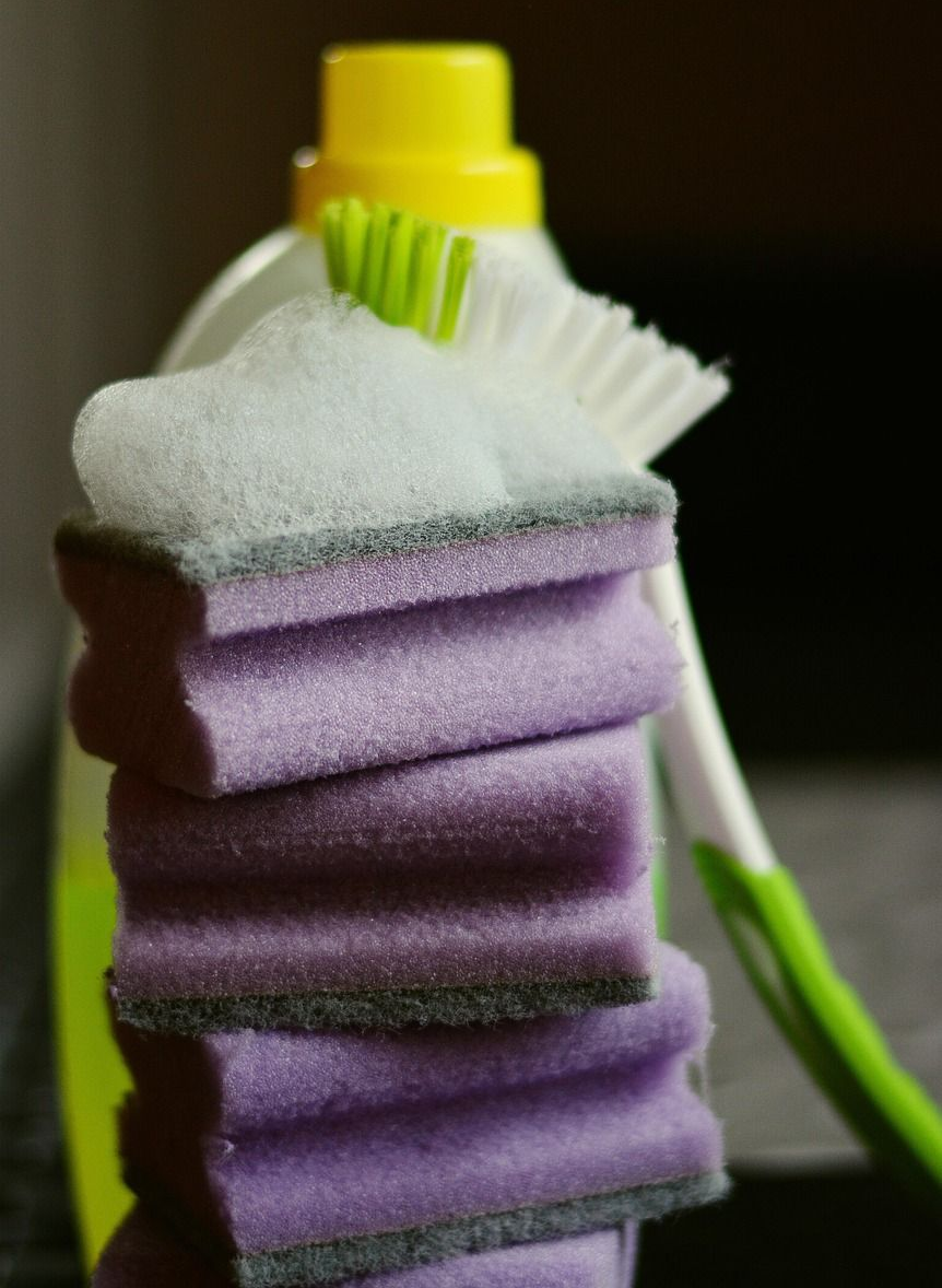Stack of purple sponges with soap, a toothbrush, and a cleaning bottle.