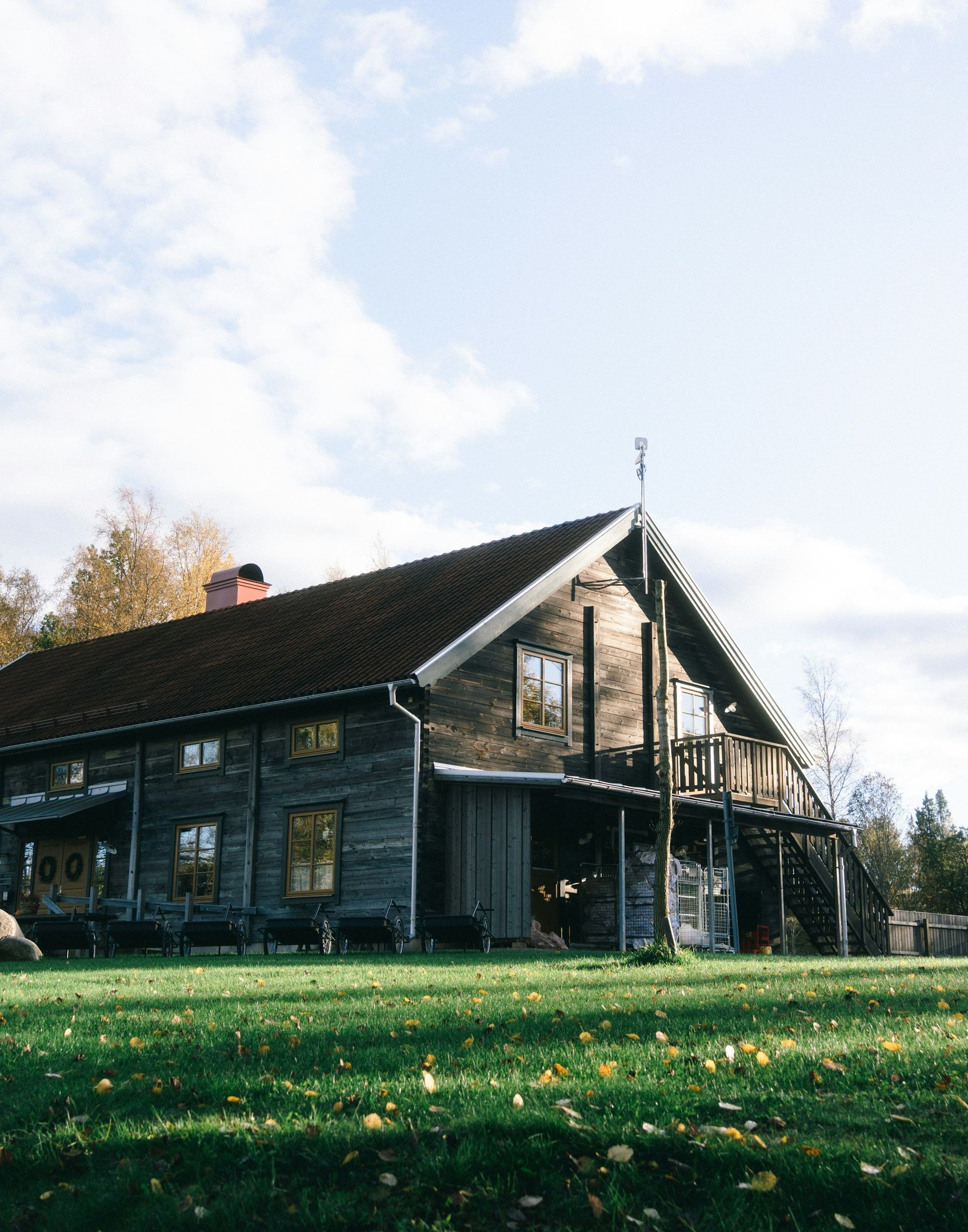 A rustic, dark-wood building with a tiled roof stands next to a green lawn on a sunny day with a bright blue sky.