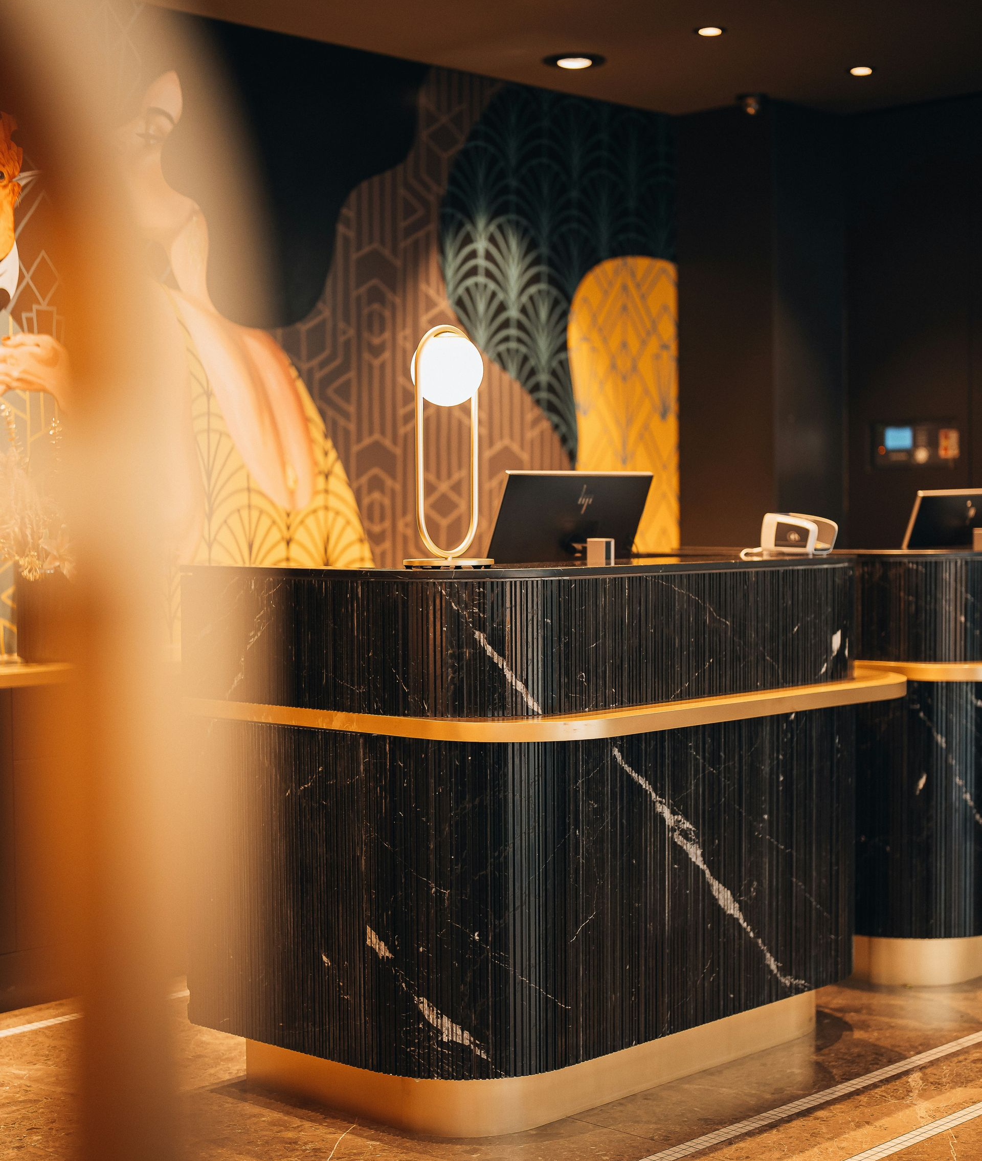 A sleek, dark marble hotel reception desk with gold trim, featuring art deco wall patterns and warm lighting.