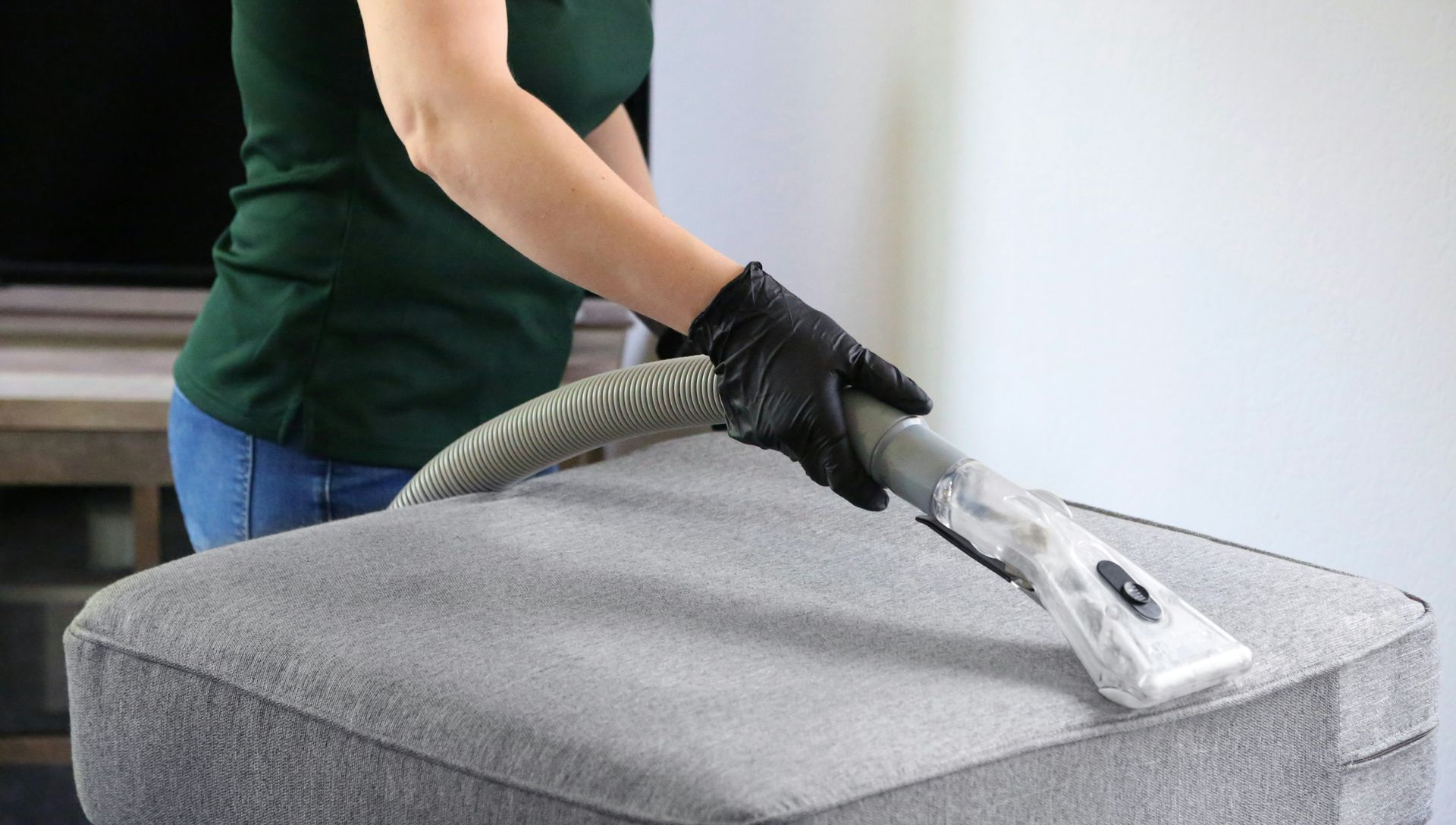 Person vacuuming a gray upholstered ottoman with a handheld upholstery tool
