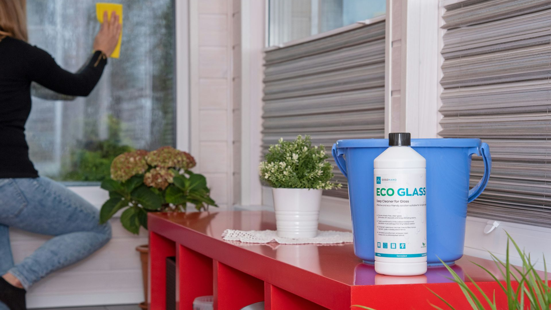 Woman cleaning window with a yellow sponge. Bottle of