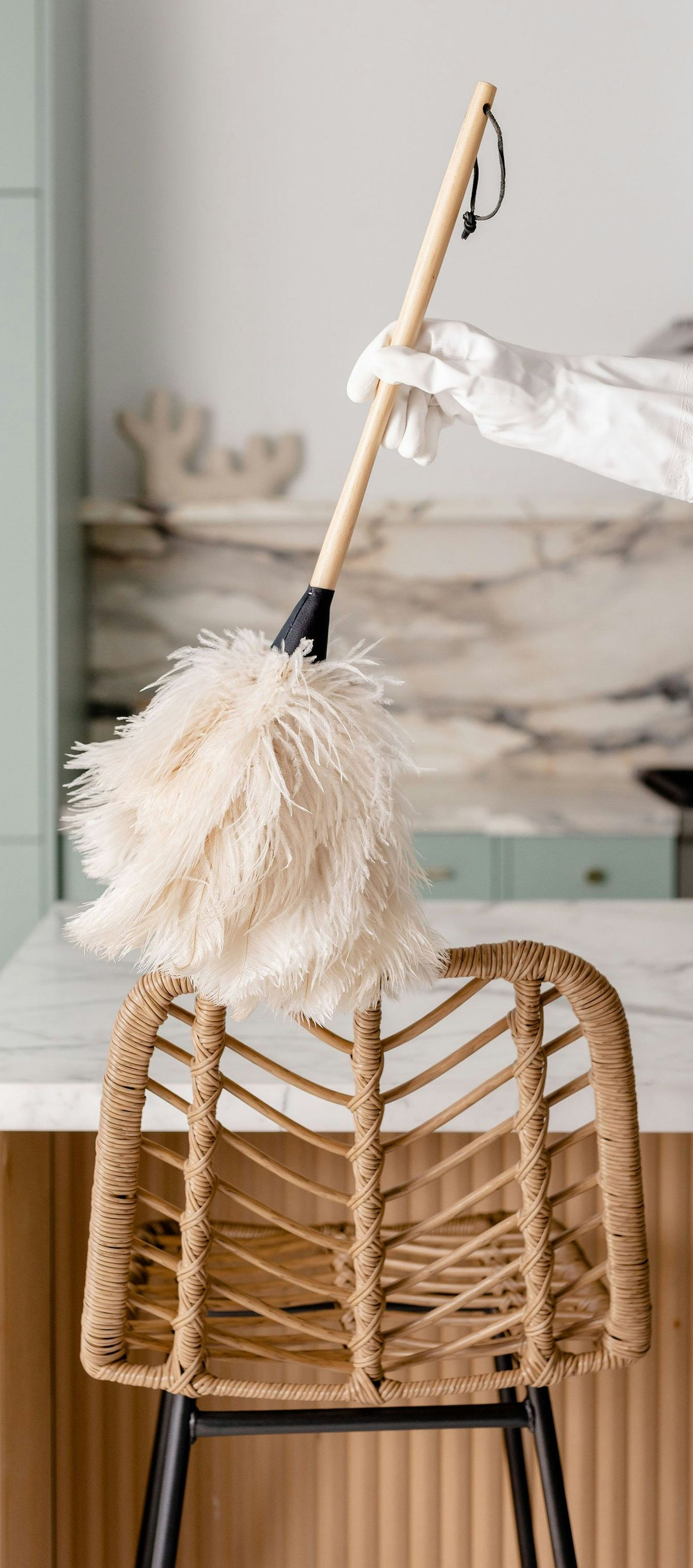 White feather duster hanging from a woven chair in a light, minimalist room