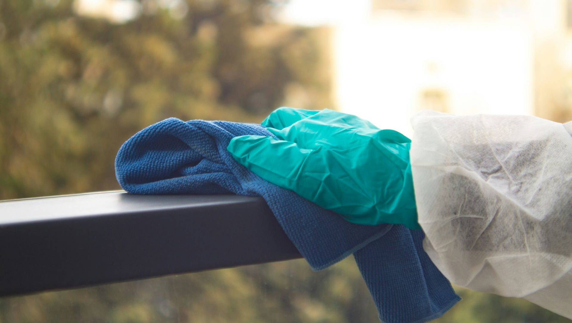 Colorful cleaning cloths draped over a black railing outdoors, with blurred trees and buildings in the background