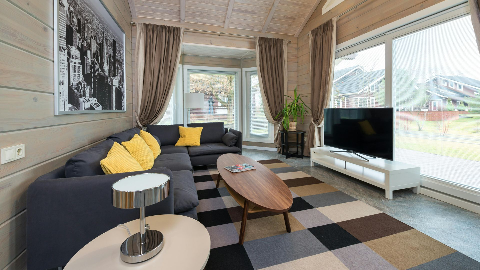 Living room with a gray sectional, yellow pillows, and large windows. A black and white photo hangs on the wall.