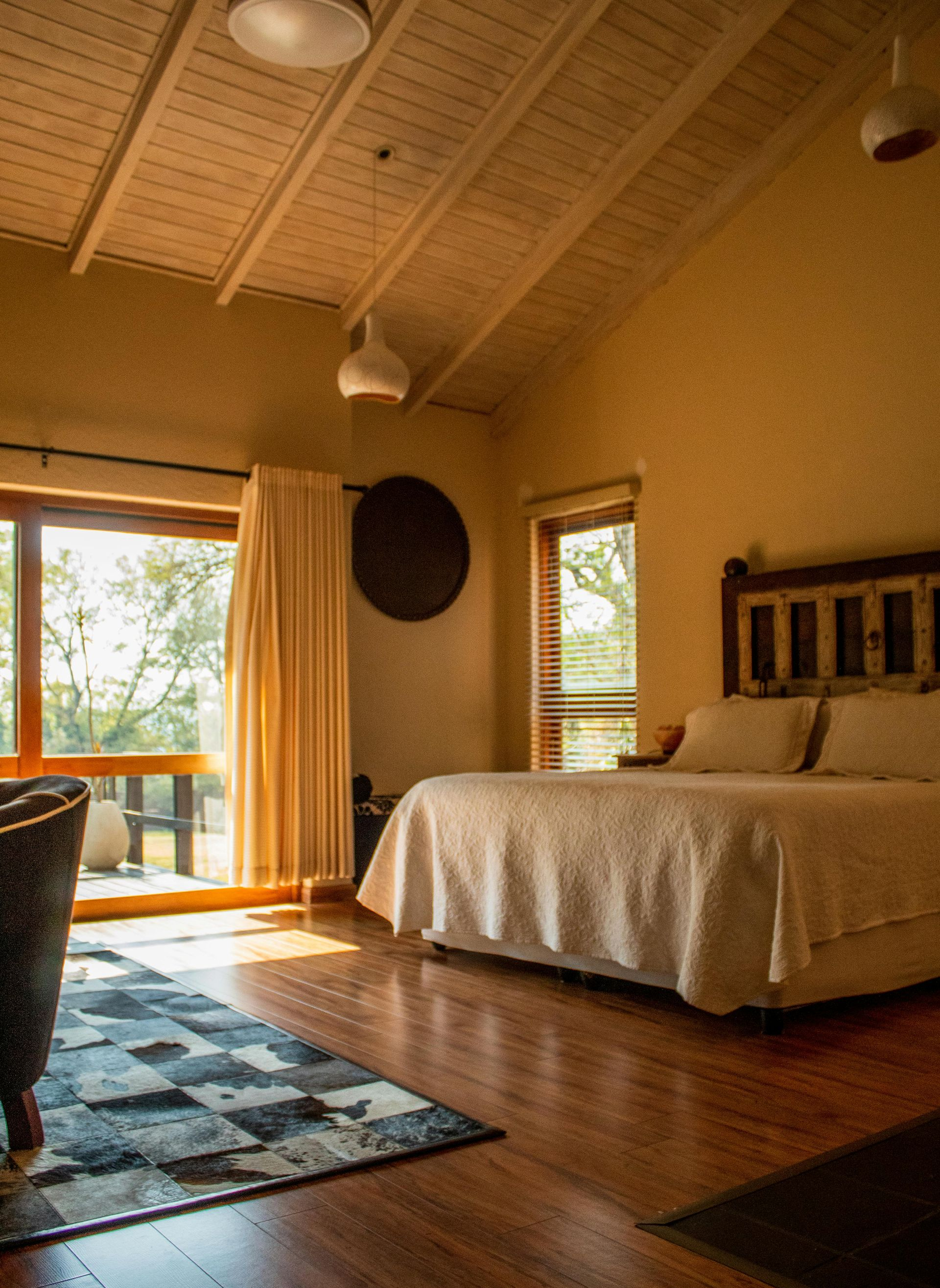 Bedroom with a bed, rug, window, and wooden ceiling. Warm lighting and natural views.