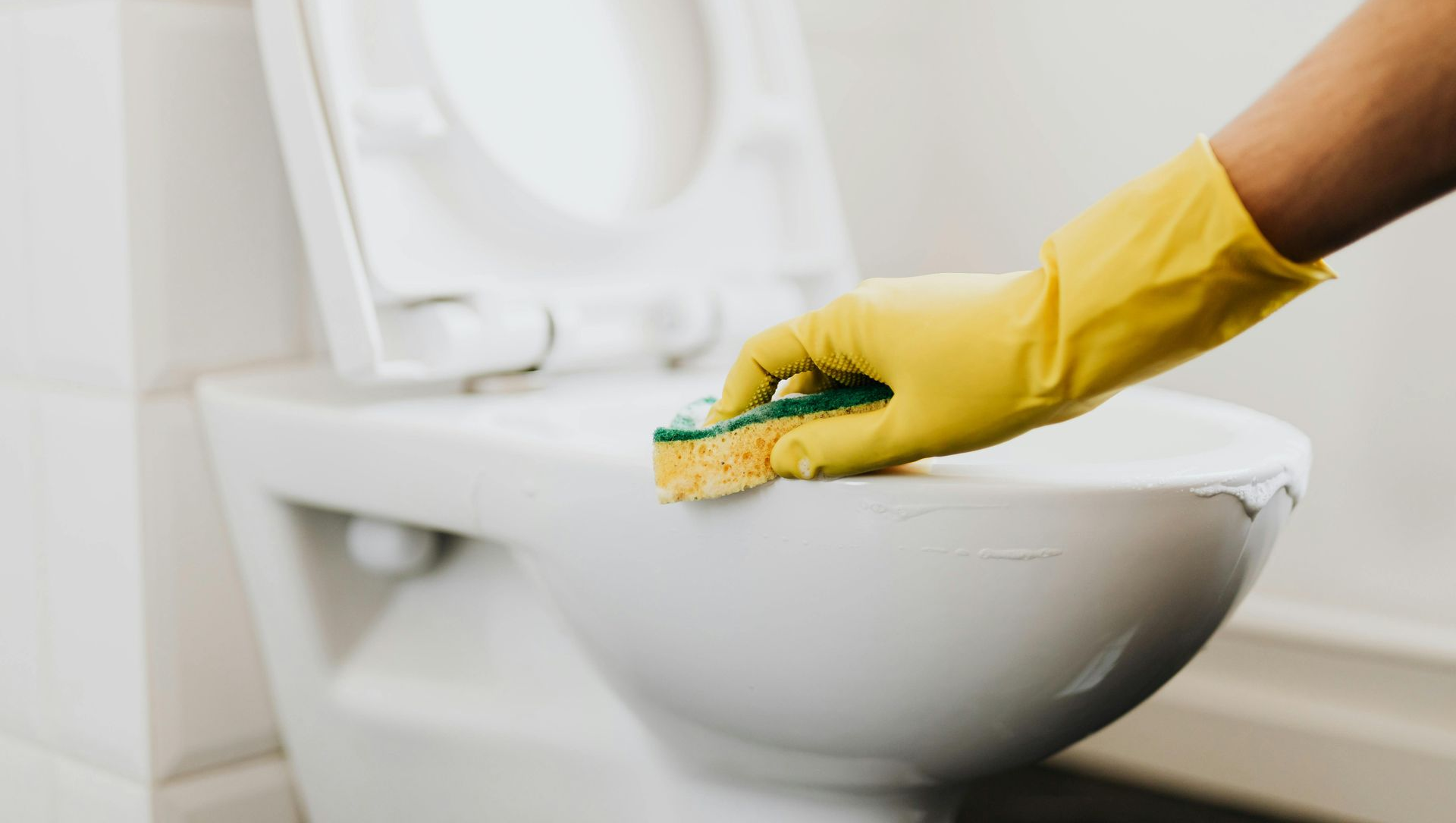 Person in yellow glove scrubs a white toilet with a sponge.