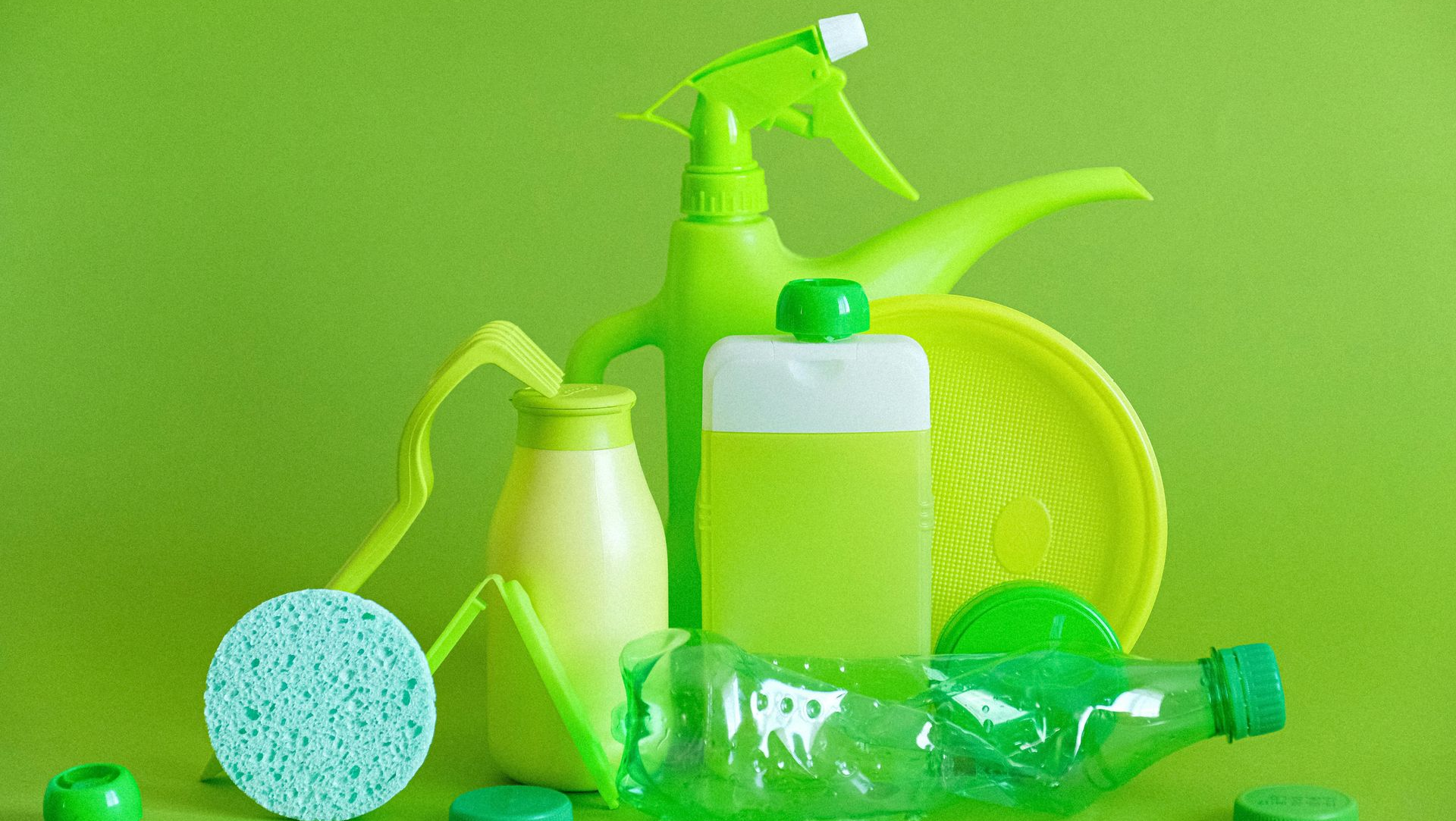 Assortment of green cleaning supplies, including bottles, a sponge, and a watering can, against a green background.