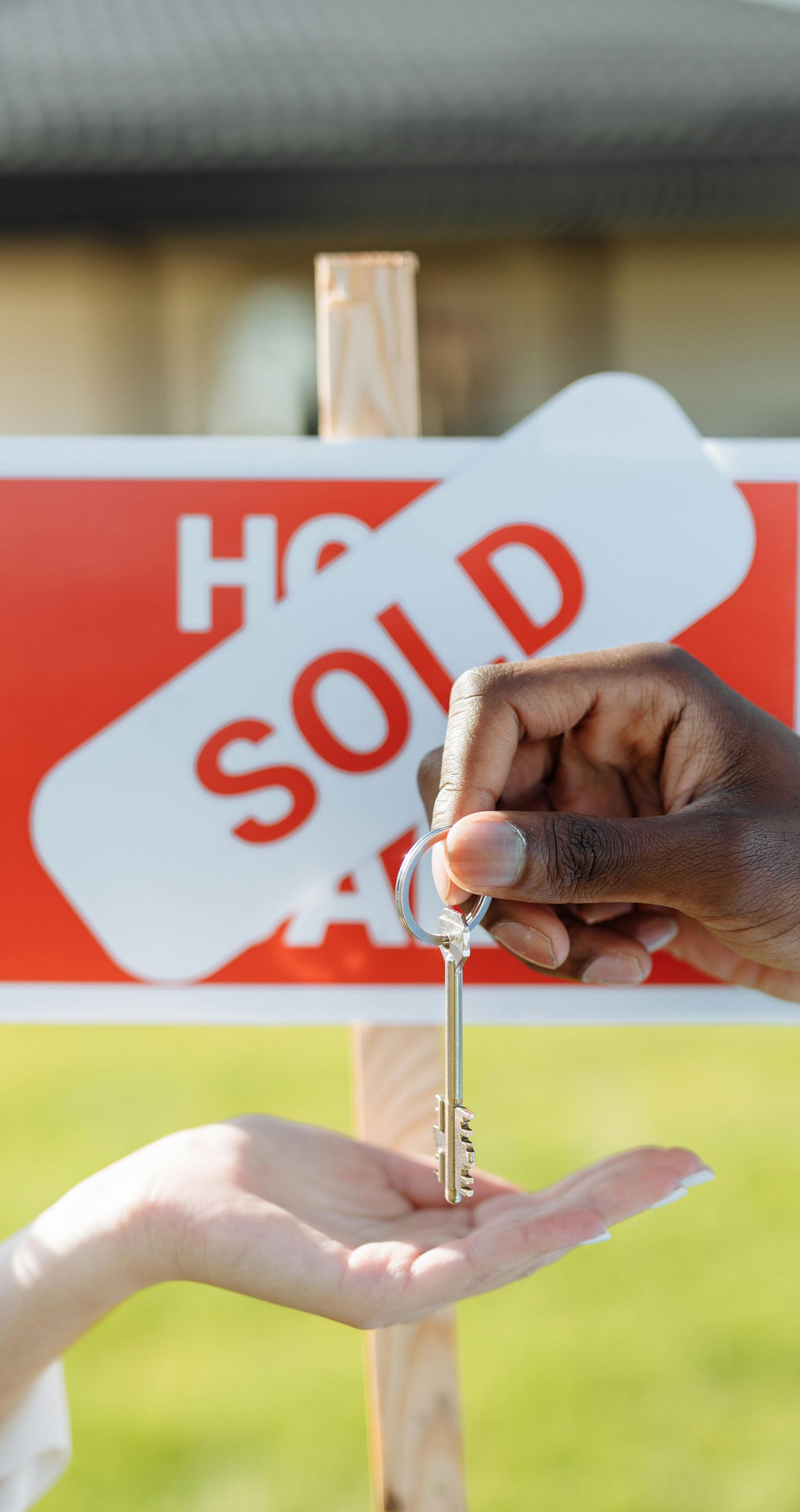 Handing over house keys in front of a “SOLD” sign.