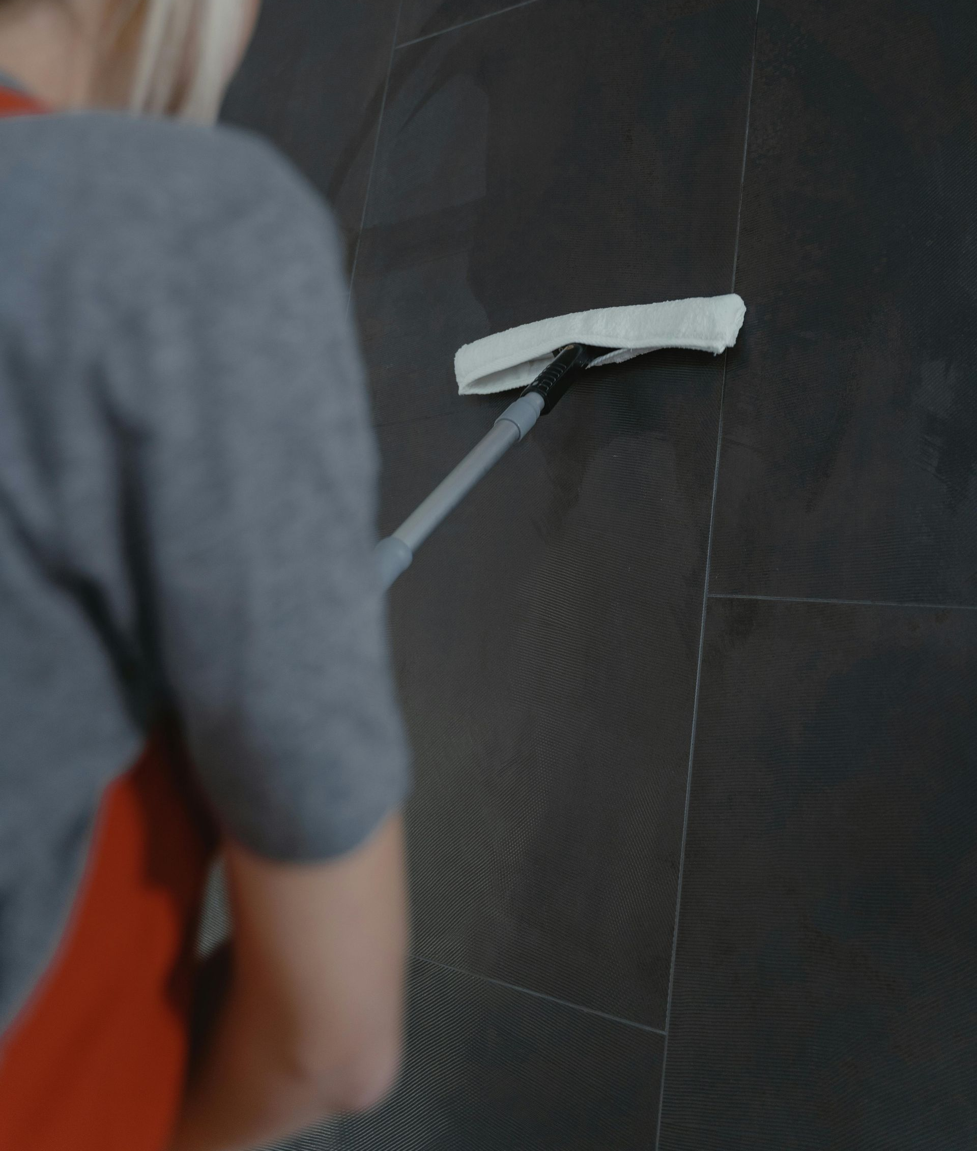 Person cleaning dark tiled wall with a long-handled squeegee.