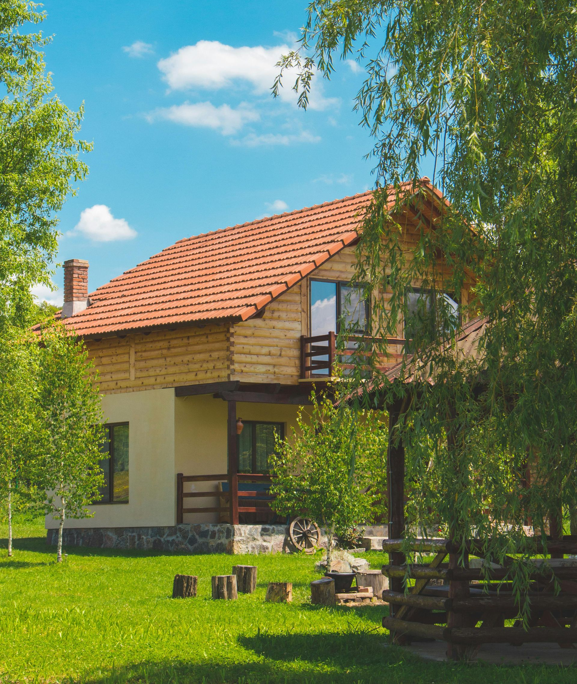 Two-story house with a red tile roof and wooden accents, set in a grassy yard under a blue sky.