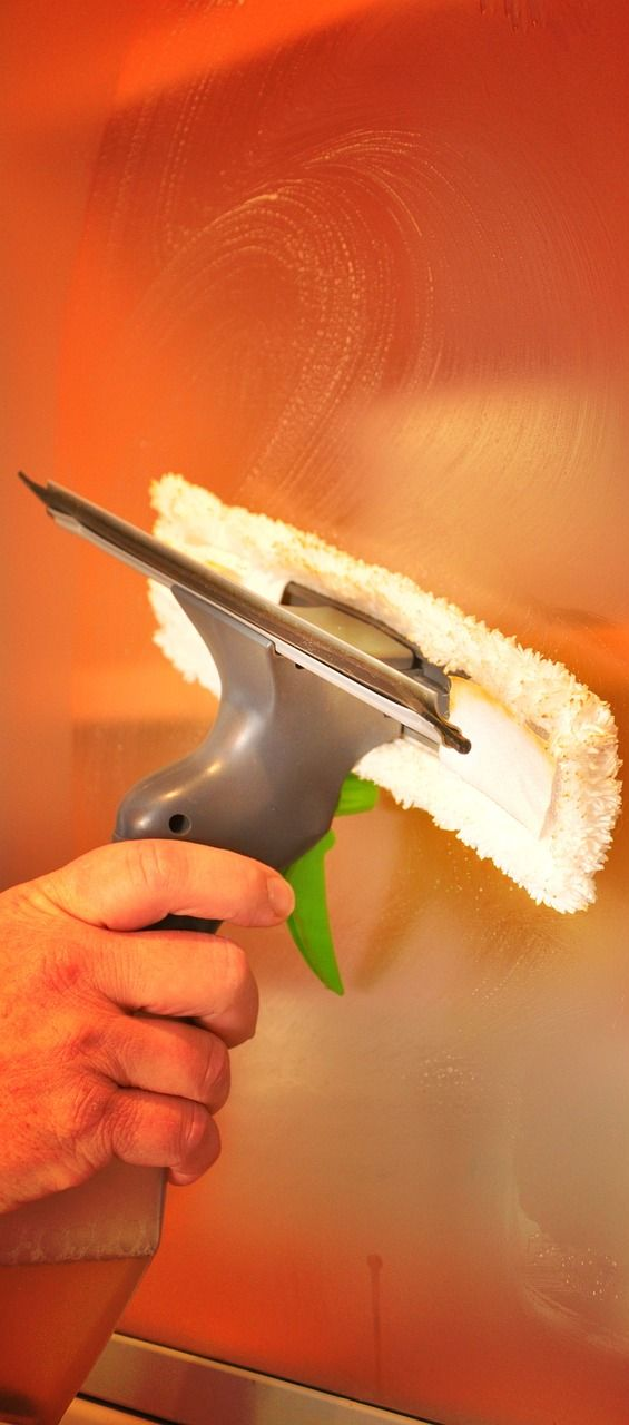 A person's hand using a window washing tool on an orange surface.