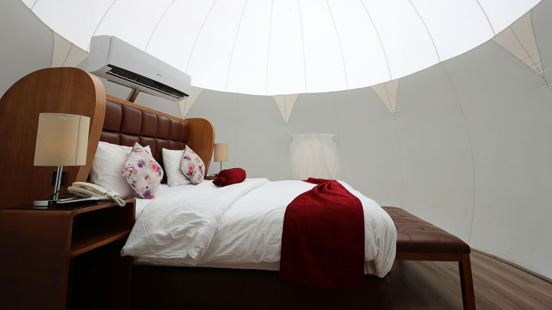 Bedroom with white dome ceiling, bed with red throw, nightstand with lamp, and air conditioning unit.