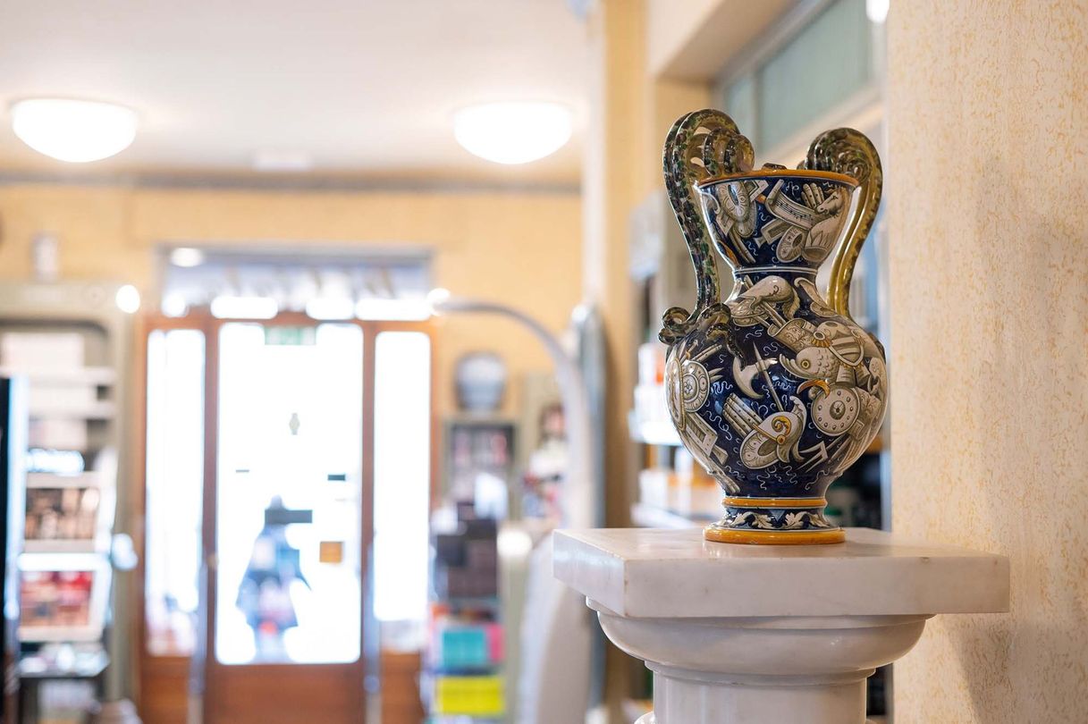 All'interno di una boutique luminosa e sfocata, un elaborato vaso in ceramica blu e bianca poggia su un piedistallo di pietra.