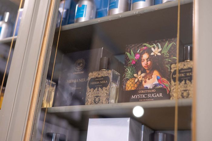 Una persona in camice bianco, con le braccia incrociate, tiene in mano uno stetoscopio, sullo sfondo sfocato di una farmacia.