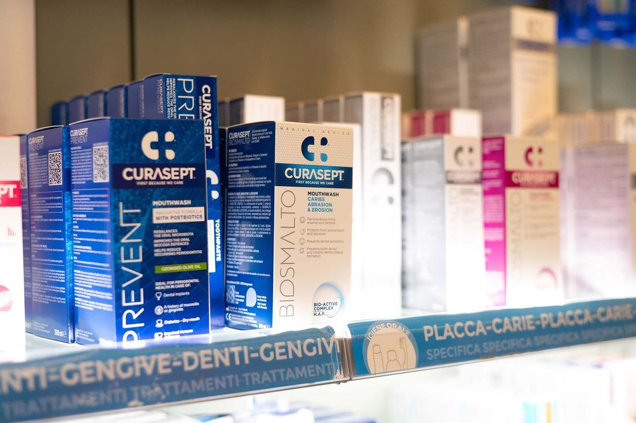 Scaffale pieno di prodotti per l'igiene orale del marchio Curasept, in confezioni blu, bianche e magenta.