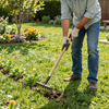 Una persona con i guanti usa un rastrello a mano per ripulire un'aiuola soleggiata dal terreno.