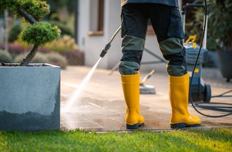 A man in yellow boots is cleaning a patio with a high pressure washer.