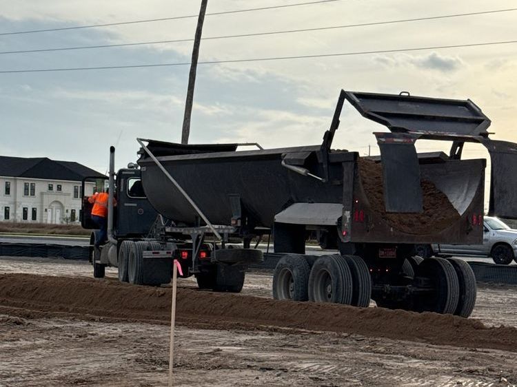A large black dump trailer dumping dirt on a construction site.