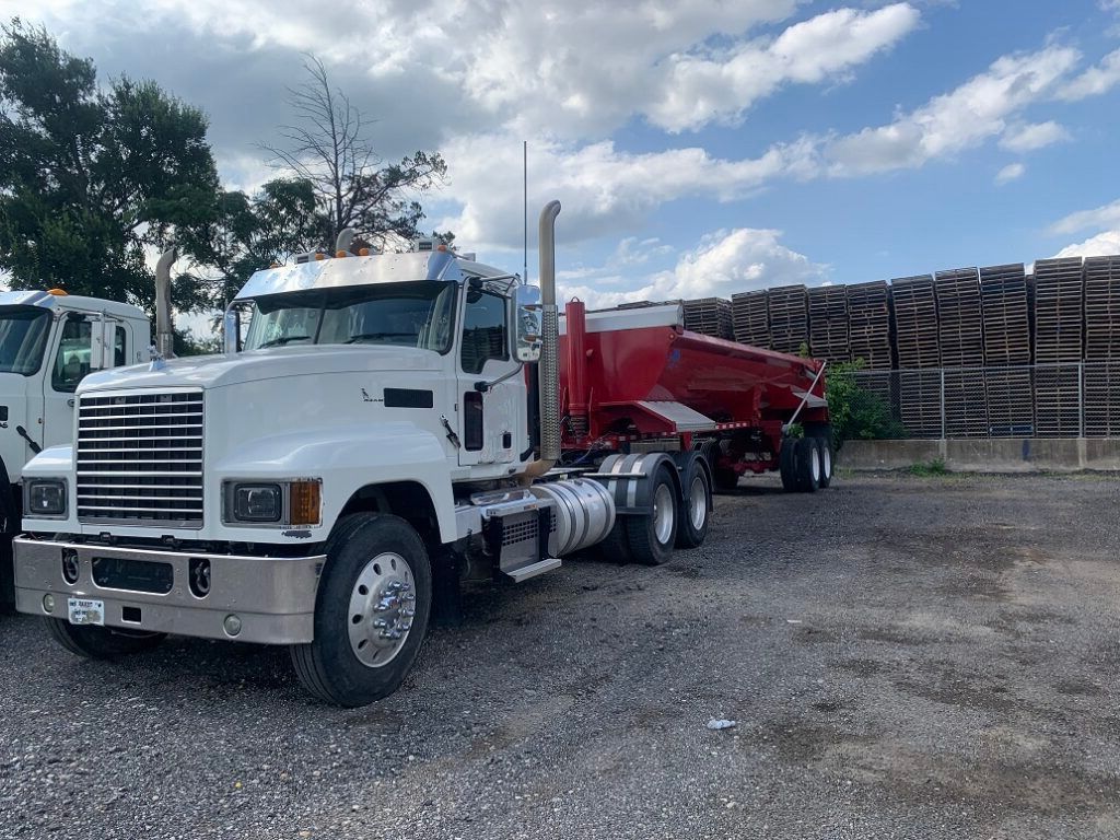 A white semi truck with a long red dump trailer on a gravel parking lot.