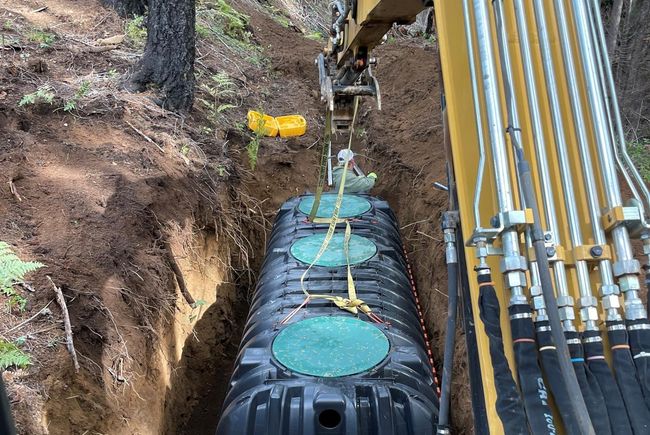 A large septic tank is being installed in a hole in the ground