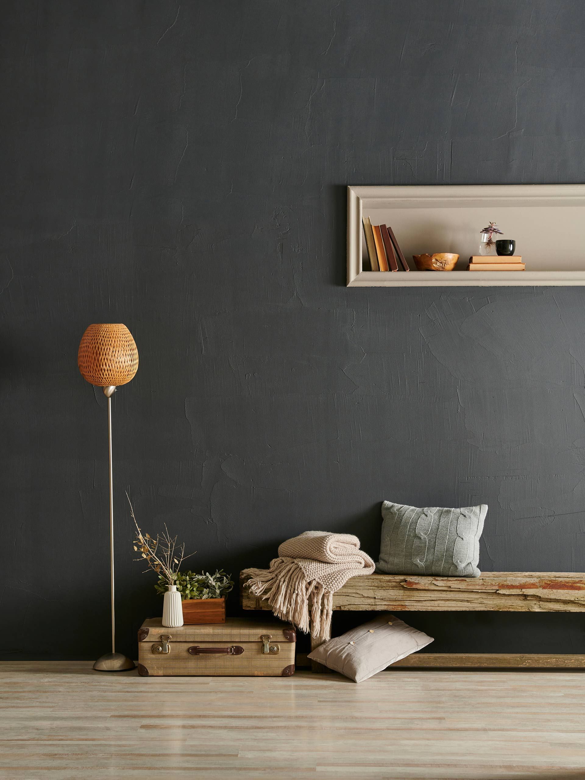 A living room with a black wall , a wooden bench , a lamp , and a shelf.