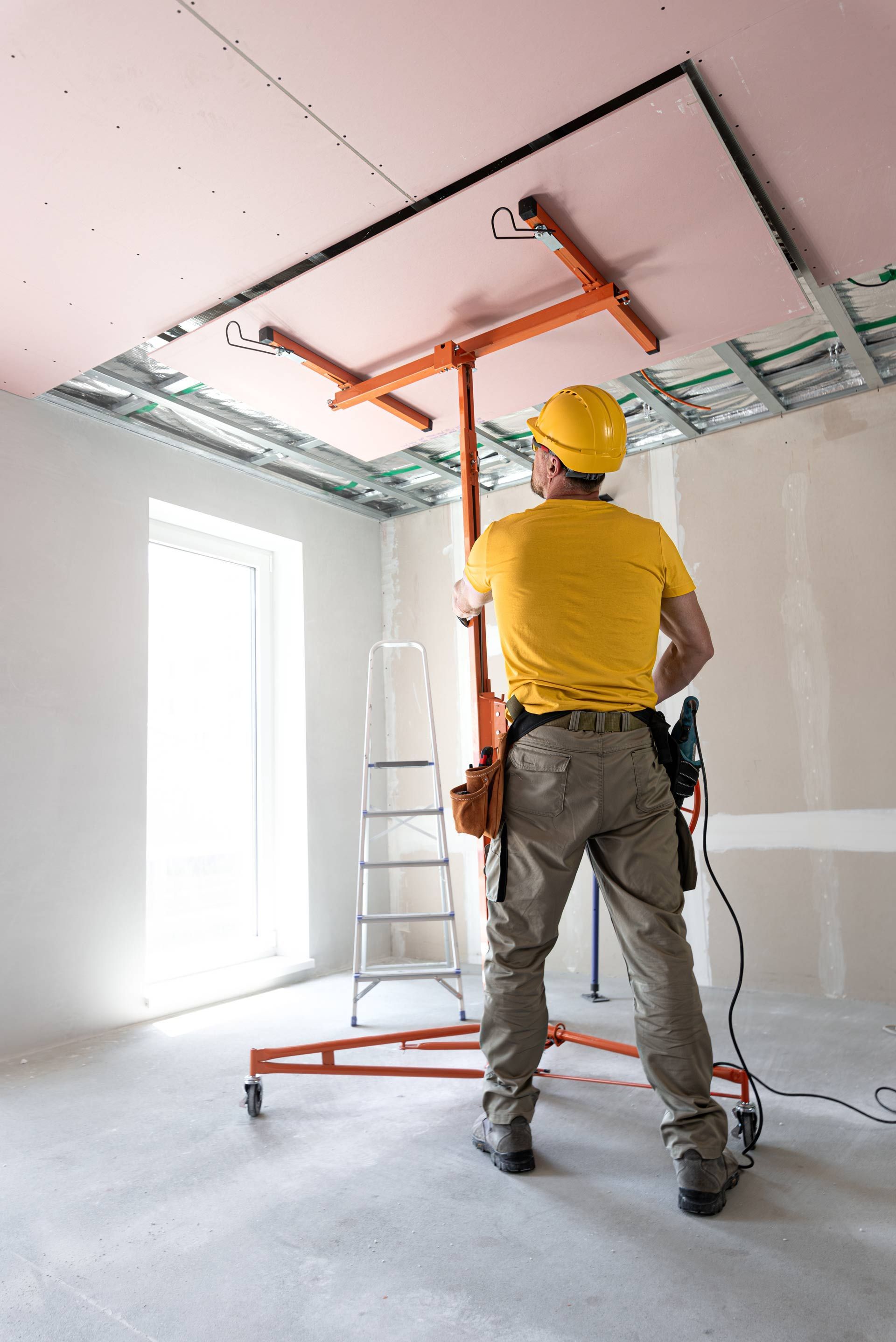 A man in a yellow shirt and hard hat is standing next to a ladder in a room.