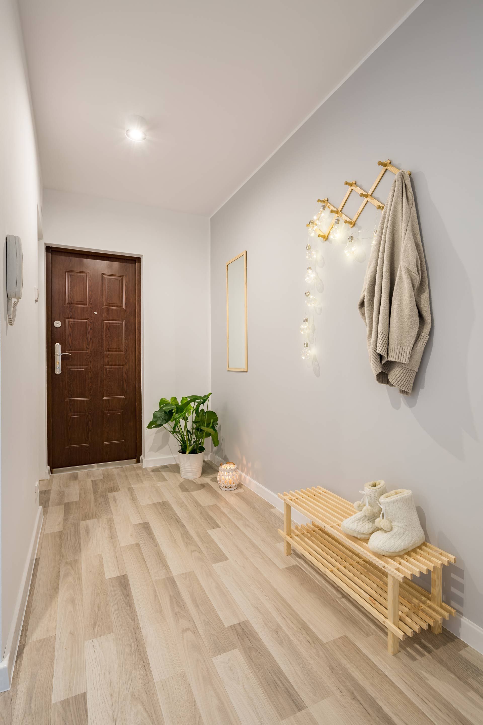 A hallway with a black door , a bench , a mirror and a coat rack.
