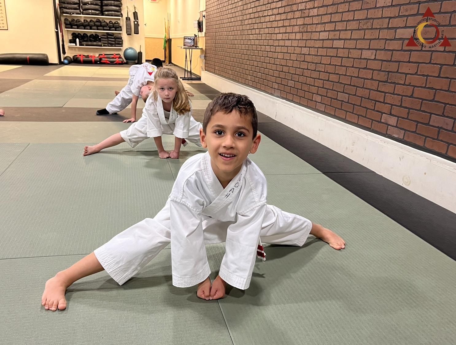 A boy and a girl are doing stretching exercises on a mat in a gym.