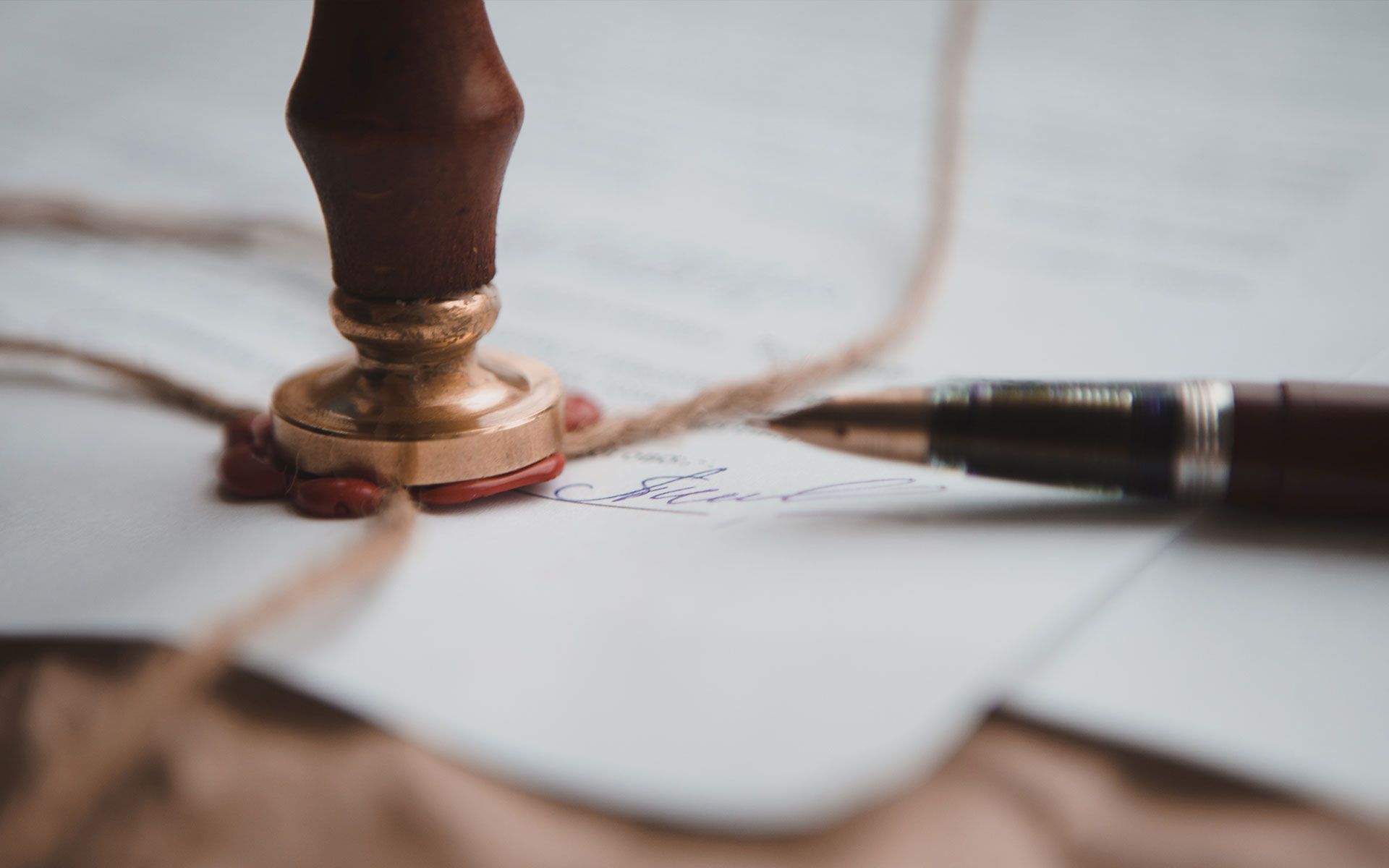 A wax seal with a wooden handle on a document, near a fountain pen, indicating approval.