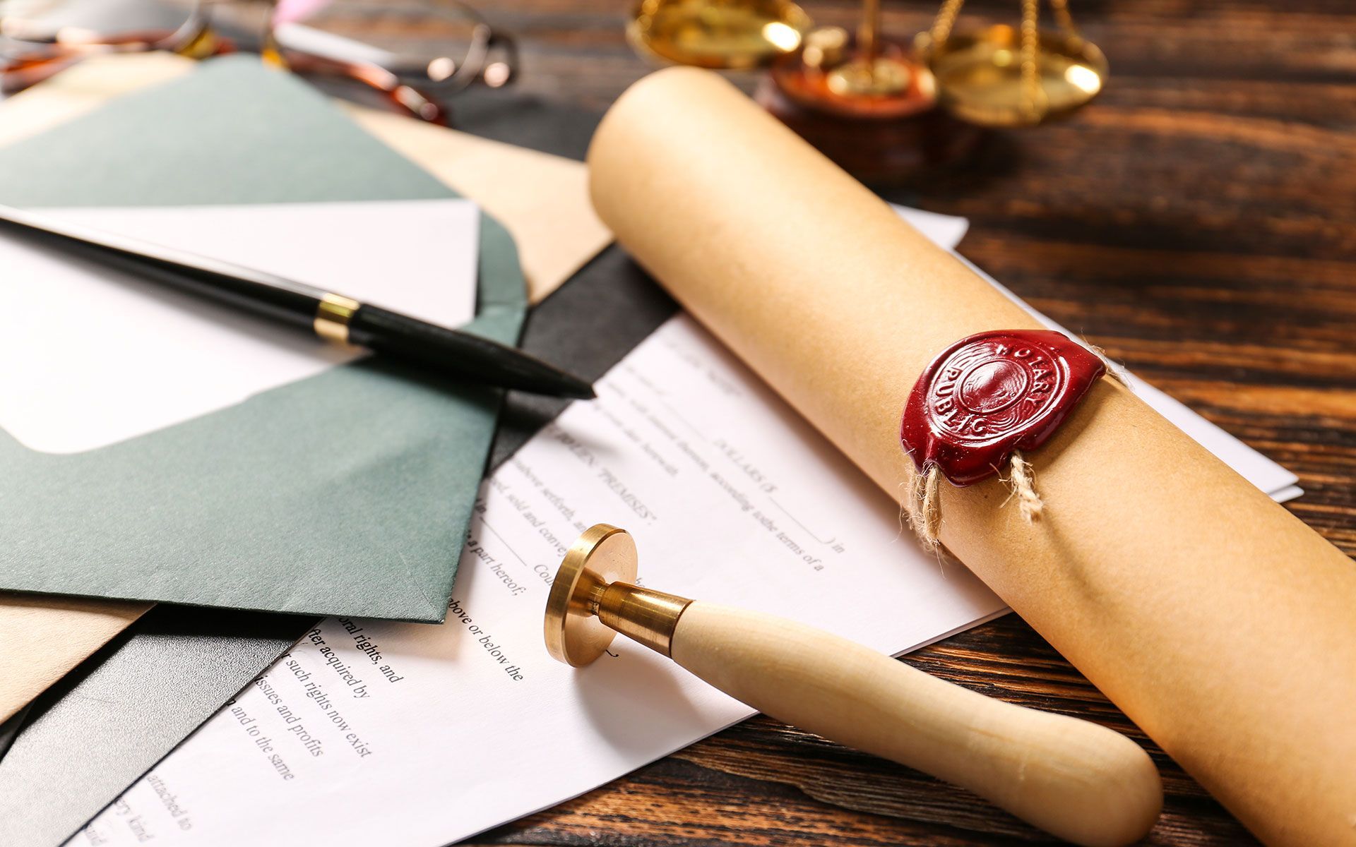 Close-up of legal documents on a wooden desk with a rolled parchment sealed with red wax, an envelope, and a scale.